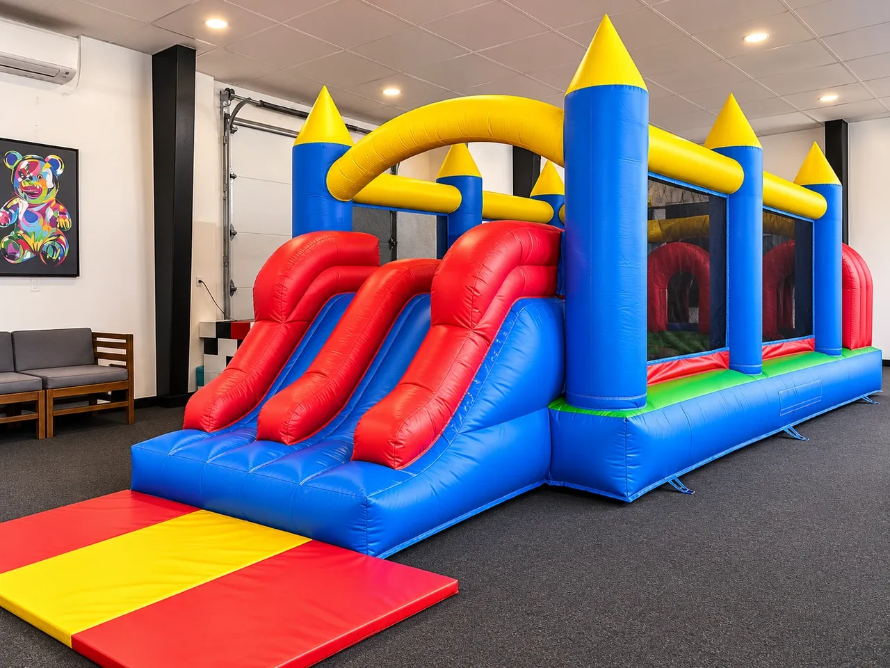 Blue, yellow, and red inflatable bounce house with a double slide, obstacle course, and landing mat.