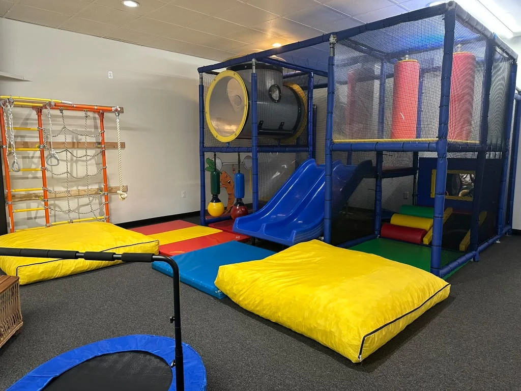 Indoor climbing structure with a tunnel, blue slide, and colorful padded mats.