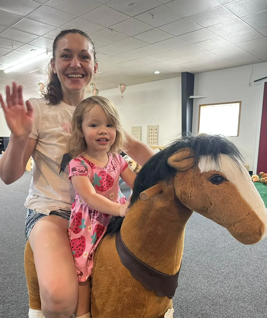 Adult and children beside a toy horse in the indoor play space.