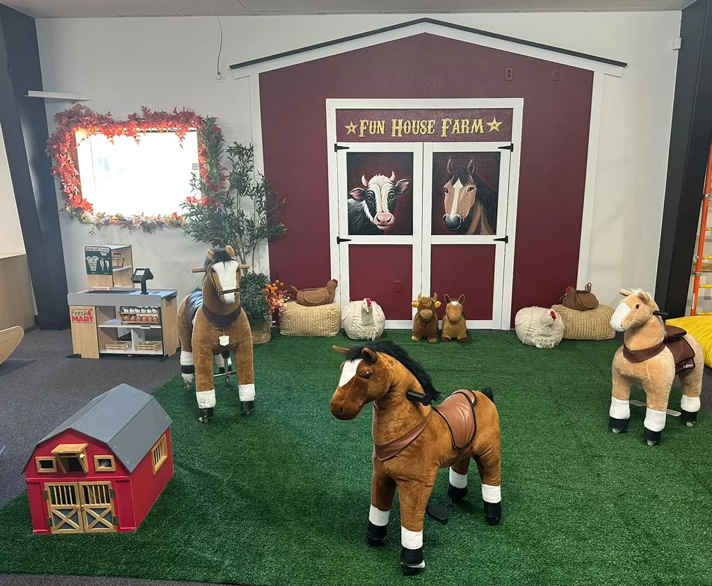 Toy horses on green flooring in front of the Fun House Farm barn backdrop.