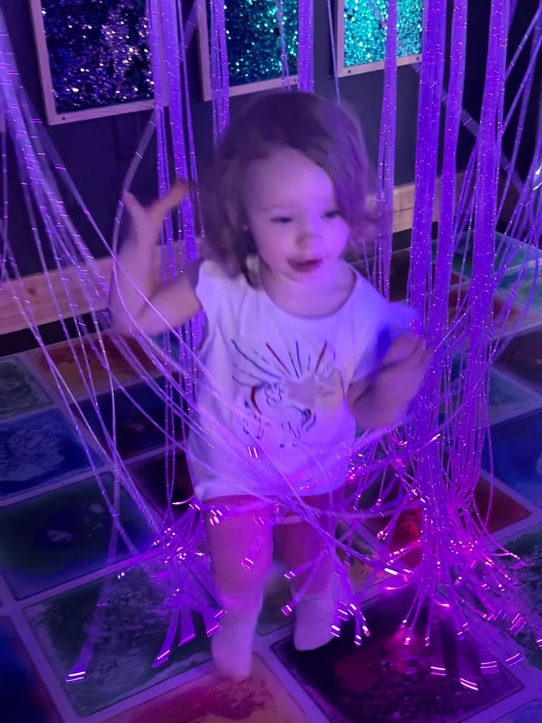 Child surrounded by purple illuminated strands in the play room.