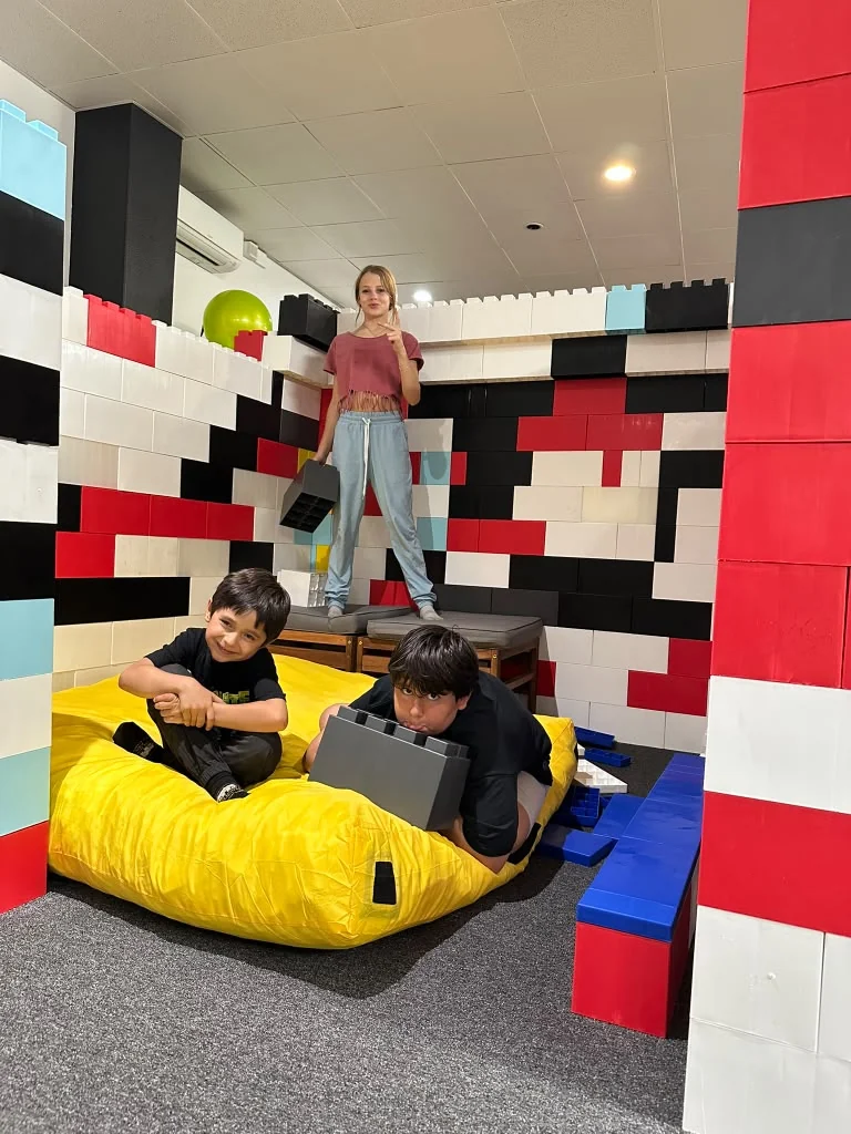 Children playing inside a structure made from large red, white, and black blocks.
