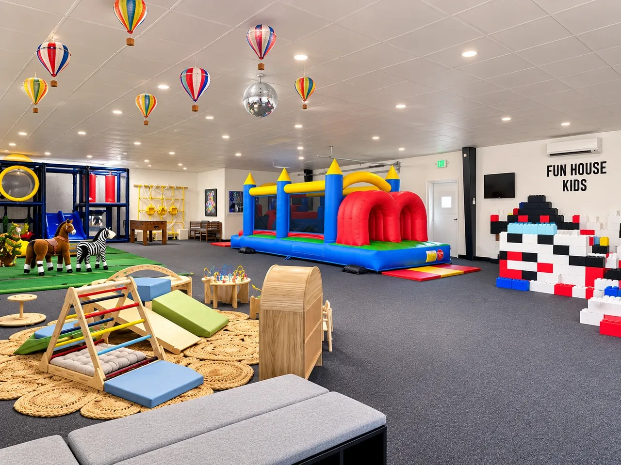 The main Fun House Kids play floor with hanging hot-air balloons, a bounce house with an obstacle course, a climbing structure, toy horses, and a giant block wall.