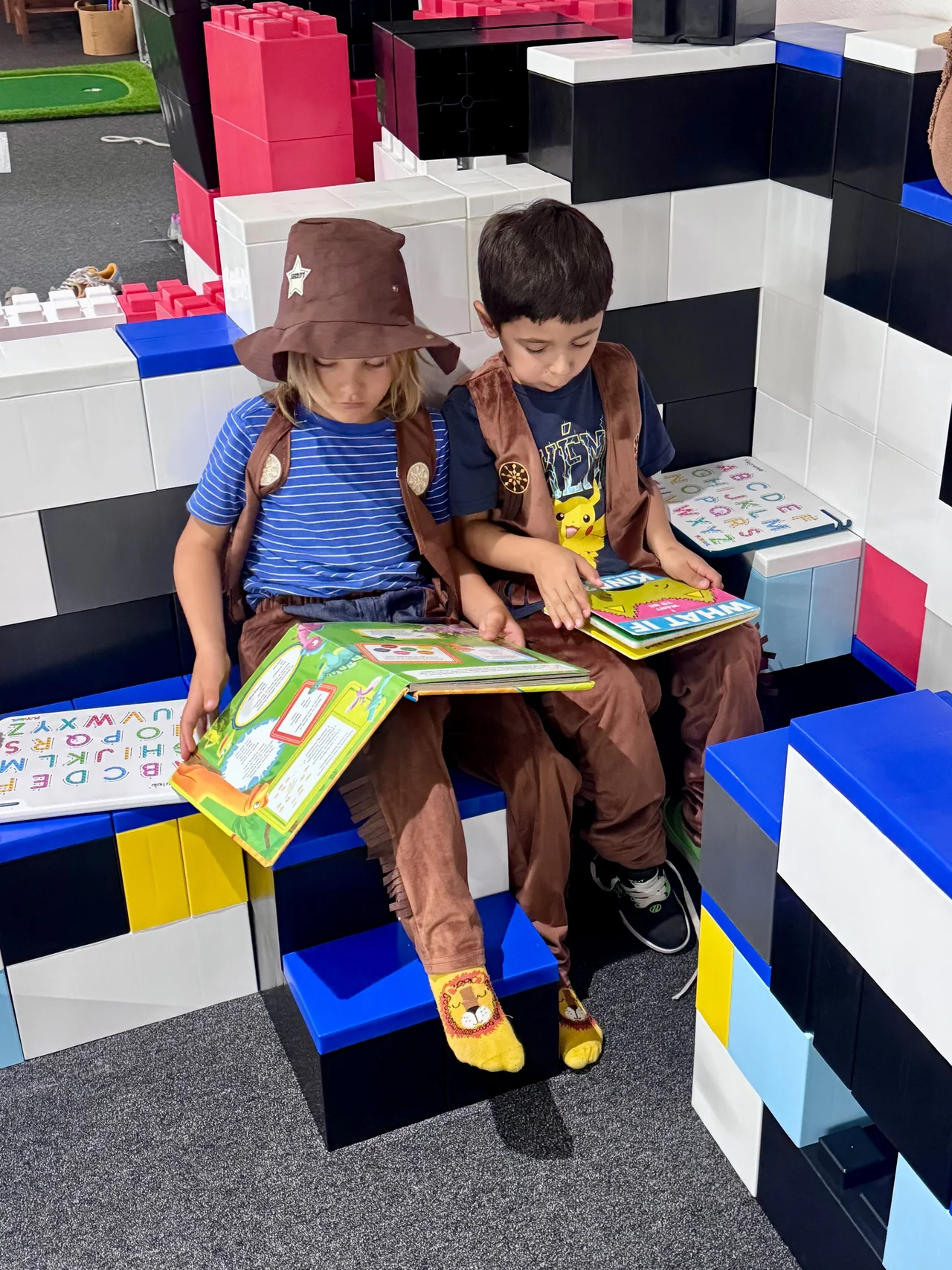 Two children reading books on a seat inside a large-block structure.