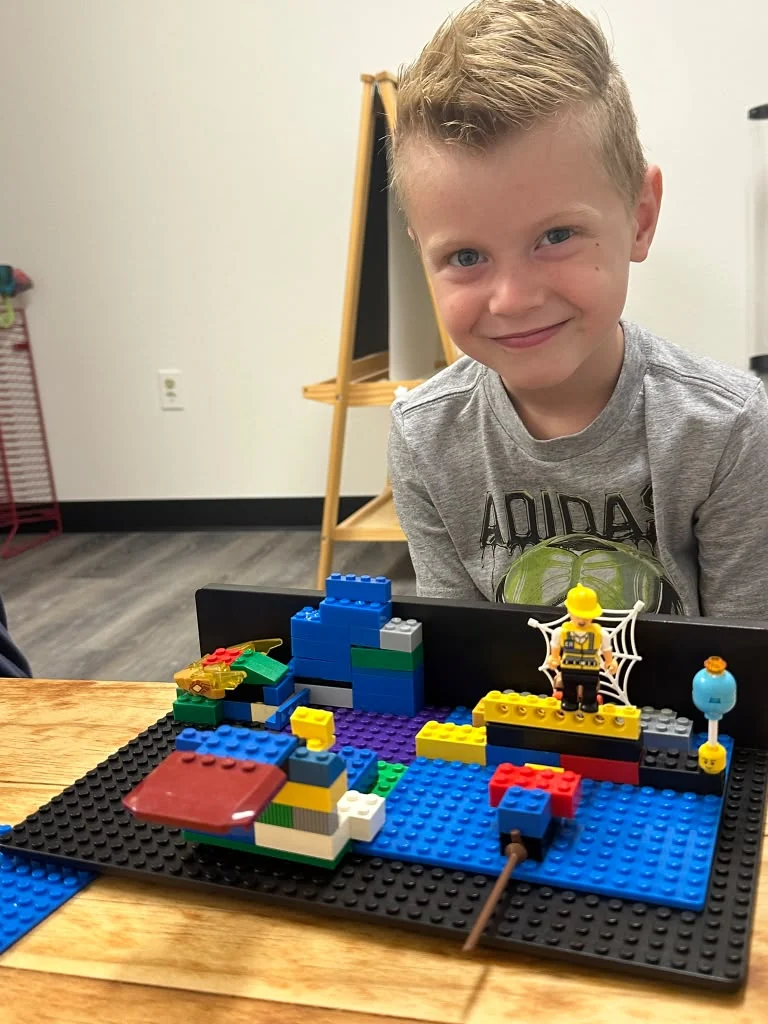 Child showing a colorful small-block creation at a table.