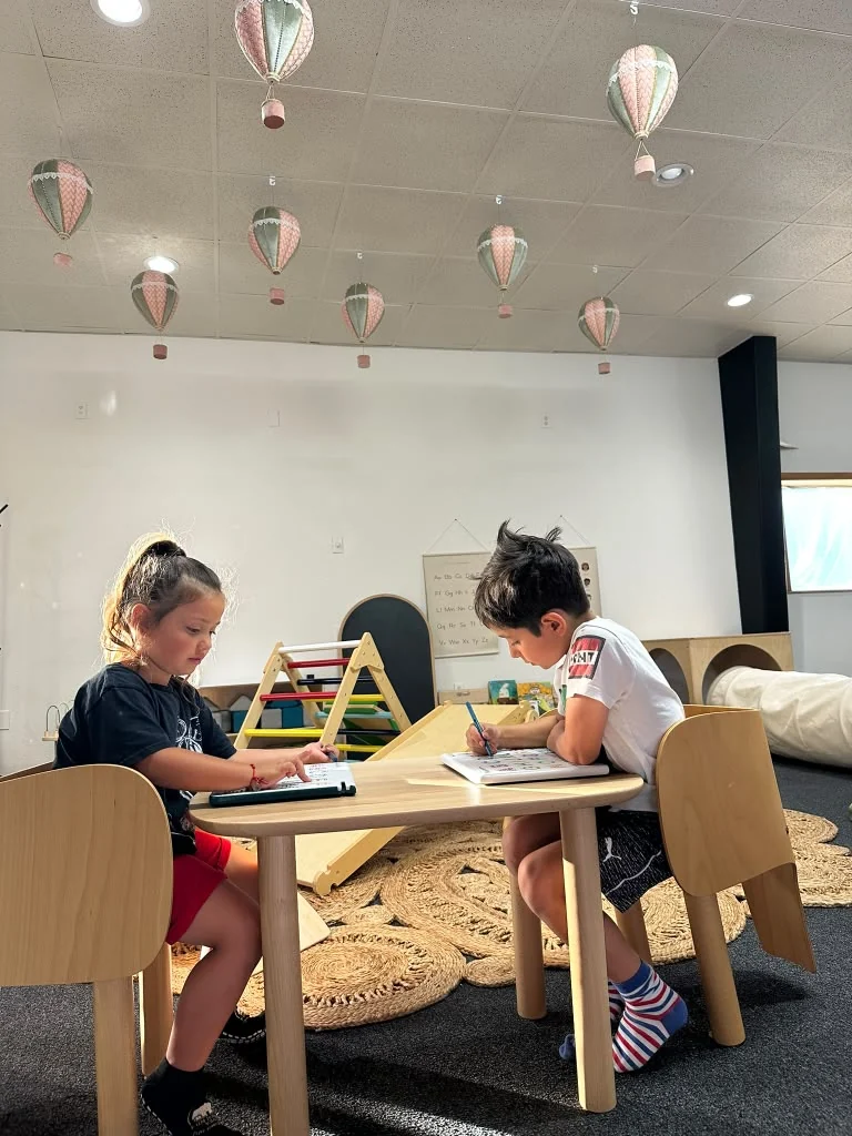 Children working on tabletop activities beneath hanging hot-air-balloon decorations.